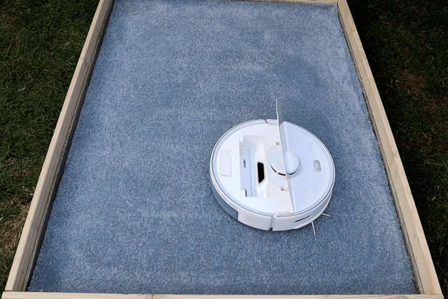 Roborock S5 Max стоит на ковре с высоким ворсом с открытым клапаном после испытания на всасывание.